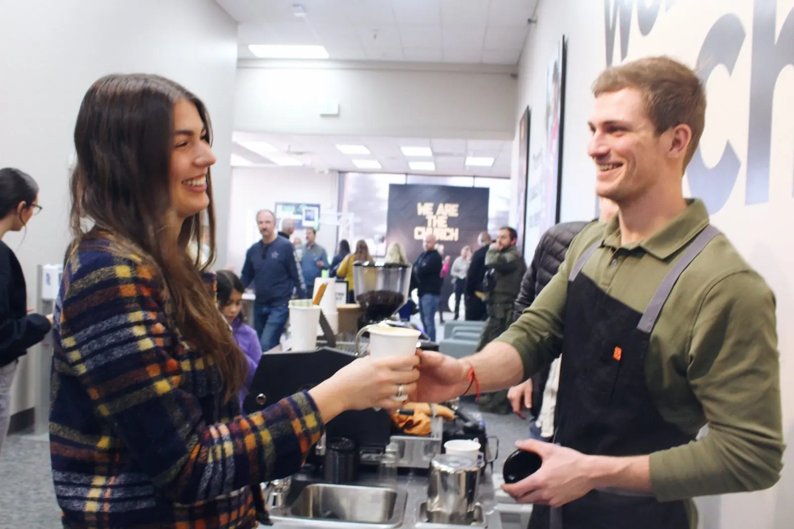 A Zado barista handing a drink to a smiling woman at a busy office event